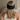 The back of a woman's head who is sitting in bed wearing a black silk sleep mask, showing how it wraps around her head. 