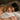 Blonde woman wearing a black silk sleep mask on her forehead, resting her head on an ivory silk pillowcase.