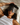 Woman with curly hair lying on a bed wearing a Dark Gray Deep Restoration silk sleep mask and resting on a white silk pillowcase, eyes covered, relaxed in soft natural light.