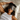 Woman with curly hair lying on a bed wearing a Dark Gray Deep Restoration silk sleep mask and resting on a white silk pillowcase, eyes covered, relaxed in soft natural light.