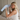 Blonde woman holding a light blue silk sleep mask showing the sculpted eye contours that protect lashes while sitting on a bed. 