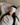Woman with long black hair lying on a bed wearing a light gray sculpted silk sleep mask and resting on a white silk pillowcase, eyes covered, relaxed in soft natural light.
