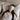 Woman with long black hair lying on a bed wearing a light gray sculpted silk sleep mask and resting on a white silk pillowcase, eyes covered, relaxed in soft natural light.