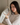 Woman holding a Light Gray Deep Restoration Silk sleep mask in her hands showing the soft, pillowy feel of it while sitting in bed.